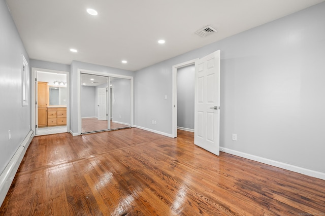 unfurnished bedroom with hardwood / wood-style floors, a baseboard radiator, a closet, and connected bathroom