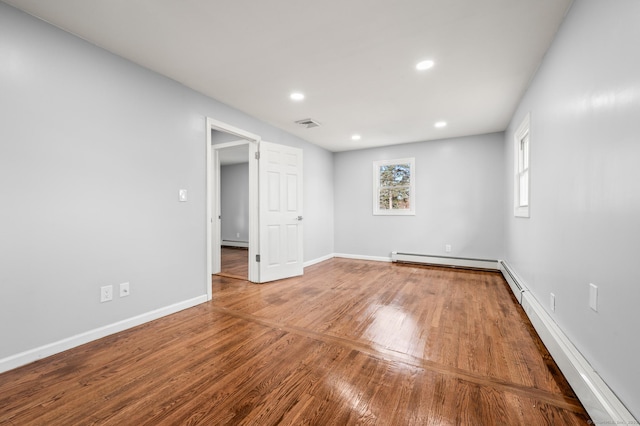 unfurnished room featuring a baseboard heating unit and hardwood / wood-style floors