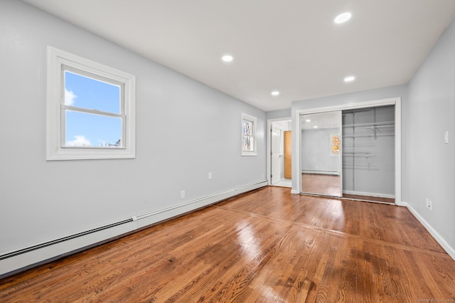 unfurnished bedroom with wood-type flooring and a baseboard heating unit