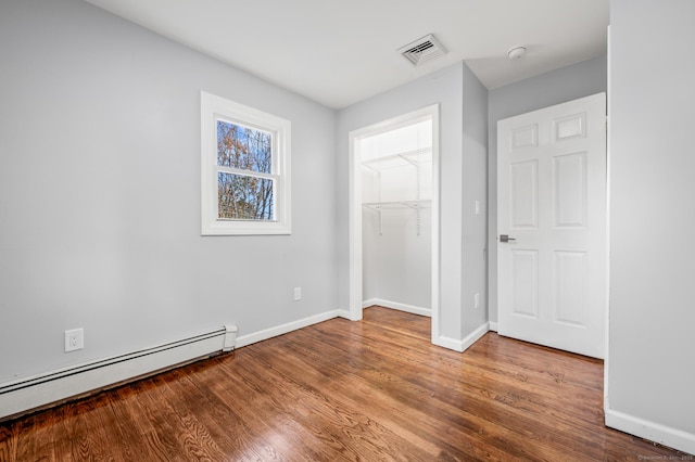 unfurnished bedroom featuring wood-type flooring, a baseboard radiator, and a closet