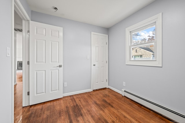 unfurnished bedroom with baseboard heating and dark hardwood / wood-style floors