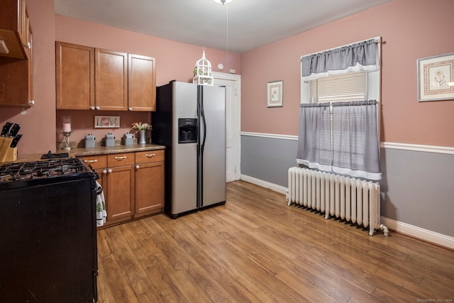 kitchen featuring stainless steel fridge, light wood-type flooring, radiator, black gas range oven, and decorative light fixtures