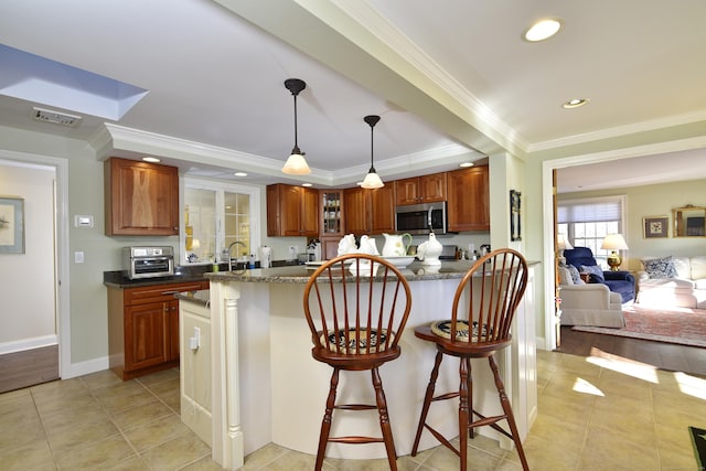 kitchen with a kitchen breakfast bar, dark stone counters, ornamental molding, decorative light fixtures, and light hardwood / wood-style flooring