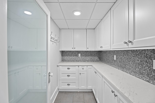 kitchen with light stone countertops, light tile patterned floors, white cabinets, and backsplash