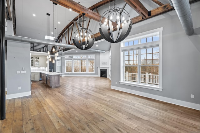 unfurnished living room with beamed ceiling, sink, a high ceiling, a notable chandelier, and light hardwood / wood-style flooring