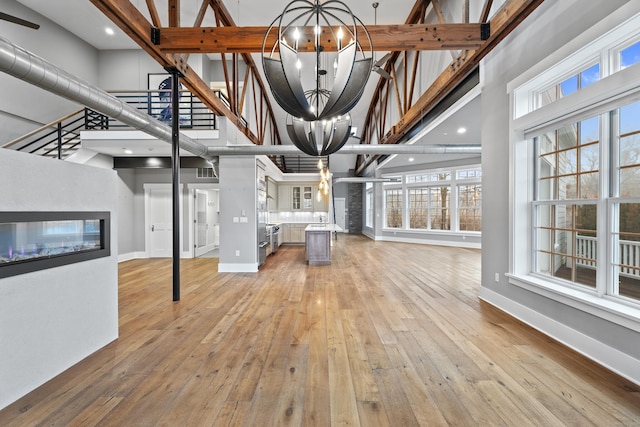 unfurnished living room with plenty of natural light, a multi sided fireplace, a high ceiling, a notable chandelier, and light hardwood / wood-style floors