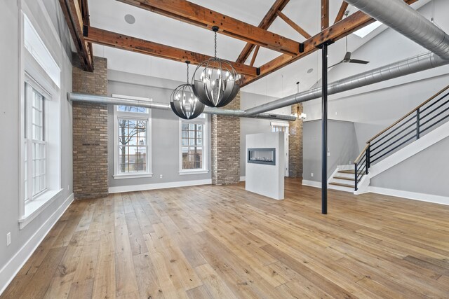 unfurnished living room with beam ceiling, brick wall, a towering ceiling, and light wood-type flooring