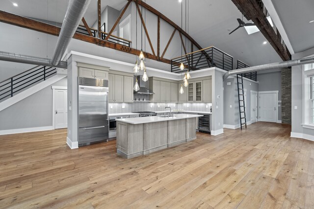 kitchen featuring decorative light fixtures, appliances with stainless steel finishes, a kitchen island with sink, and a towering ceiling