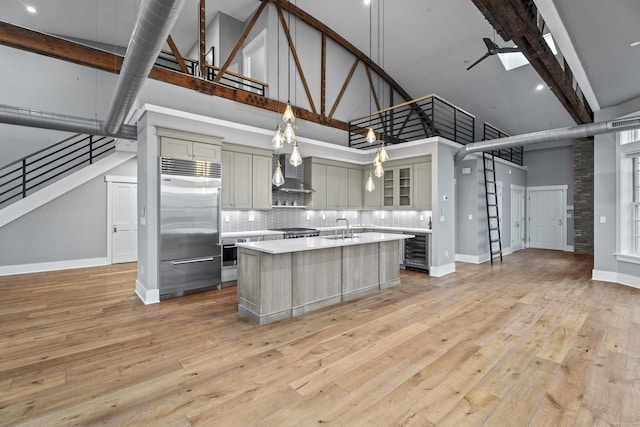 kitchen featuring stainless steel appliances, an island with sink, a towering ceiling, and pendant lighting