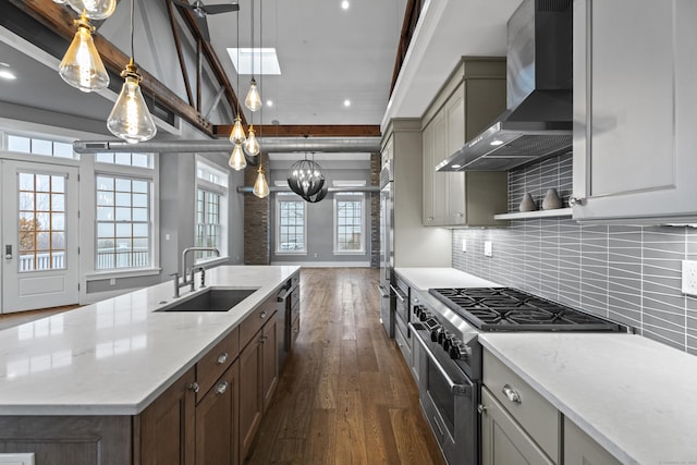 kitchen with pendant lighting, sink, light stone counters, stainless steel appliances, and wall chimney exhaust hood