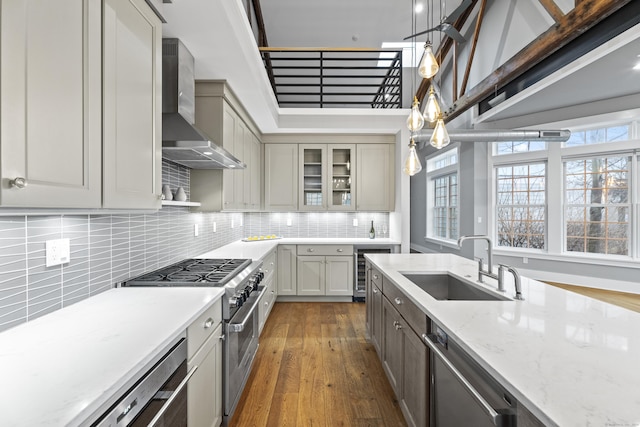 kitchen with gray cabinets, decorative light fixtures, sink, stainless steel appliances, and wall chimney range hood