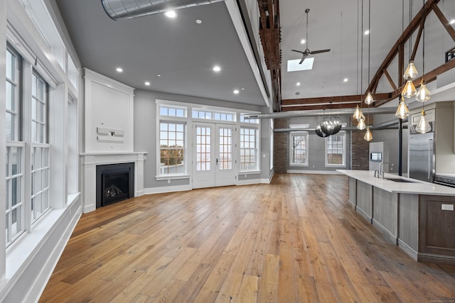 unfurnished living room with ceiling fan, sink, light wood-type flooring, and french doors