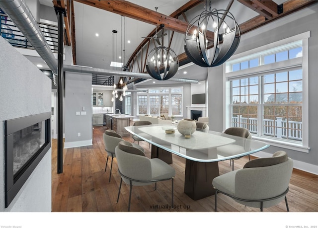 dining room with hardwood / wood-style flooring, beamed ceiling, a chandelier, and a towering ceiling