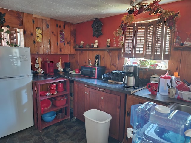 kitchen featuring white fridge, a healthy amount of sunlight, and wooden walls