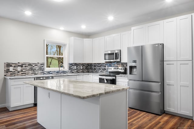 kitchen with light stone counters, a center island, white cabinets, and stainless steel appliances