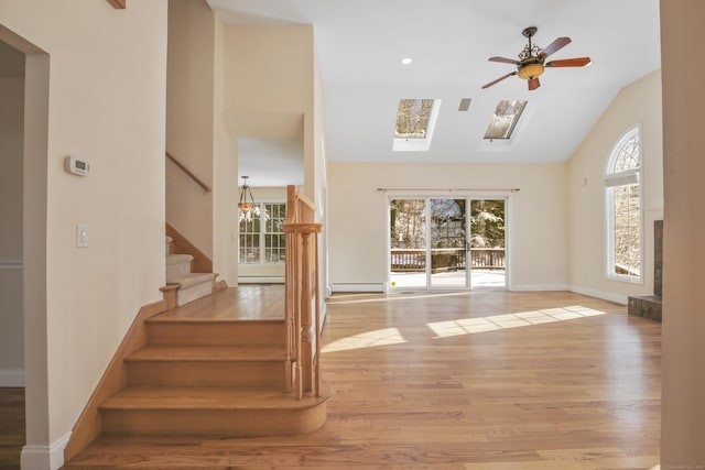 staircase with hardwood / wood-style flooring, ceiling fan, a baseboard heating unit, and vaulted ceiling with skylight