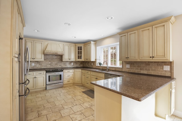 kitchen featuring custom exhaust hood, stainless steel appliances, dark stone counters, sink, and kitchen peninsula