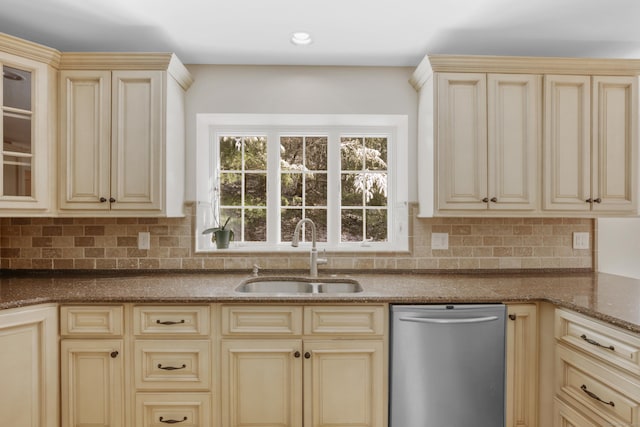 kitchen featuring sink, cream cabinetry, stainless steel dishwasher, and dark stone counters