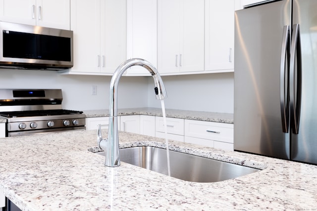 kitchen with light stone countertops, white cabinetry, sink, and appliances with stainless steel finishes