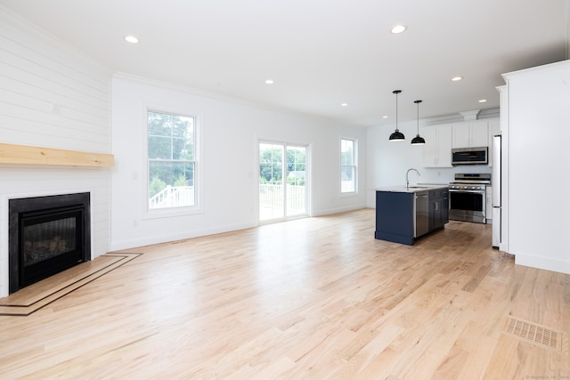 kitchen featuring appliances with stainless steel finishes, a center island with sink, decorative light fixtures, light hardwood / wood-style flooring, and white cabinetry