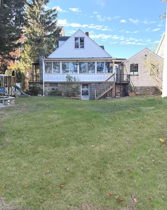 rear view of property with a lawn, a sunroom, and a playground