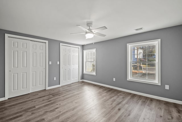 unfurnished bedroom featuring multiple closets, ceiling fan, and hardwood / wood-style flooring