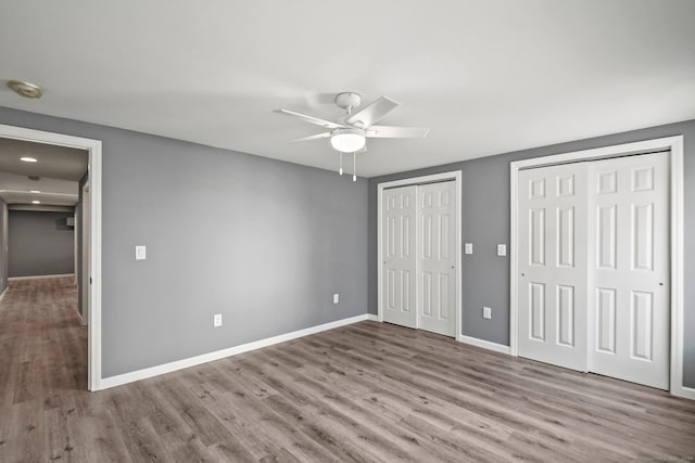 unfurnished bedroom featuring light wood-type flooring, ceiling fan, and multiple closets