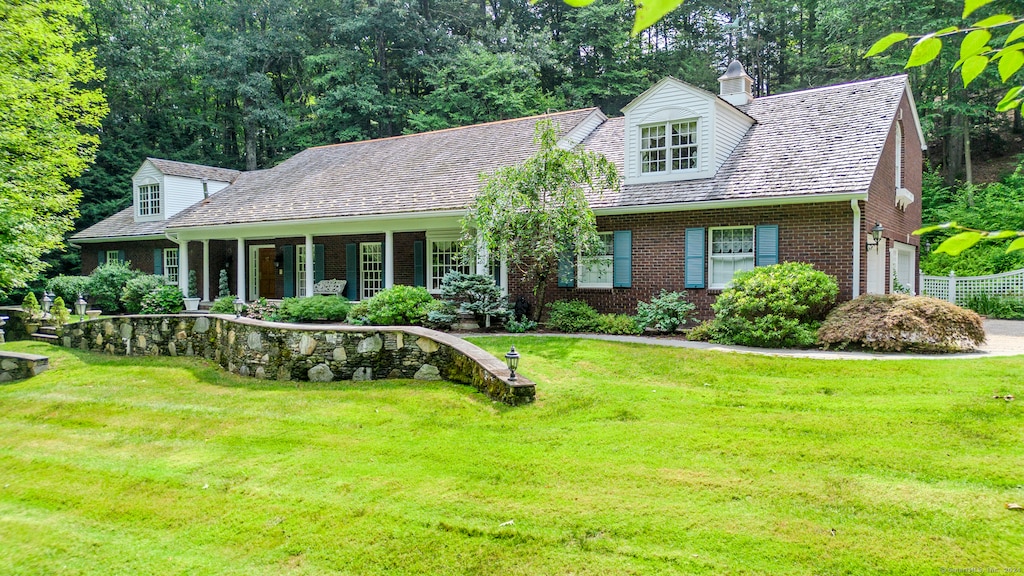 new england style home featuring a front lawn, a porch, and a garage