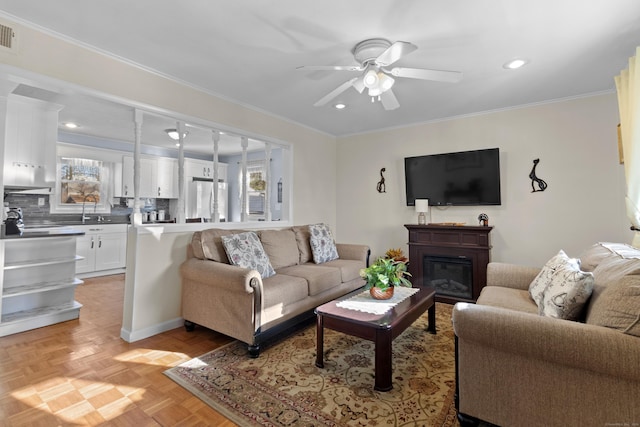 living room with light parquet floors, ceiling fan, ornamental molding, and sink