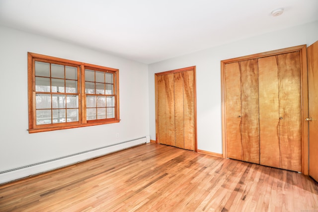 unfurnished bedroom featuring multiple closets, a baseboard radiator, and light hardwood / wood-style flooring