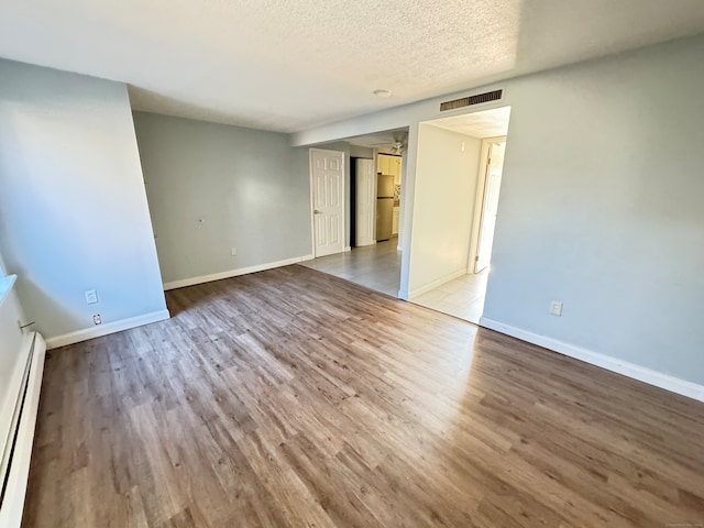 empty room featuring baseboard heating, hardwood / wood-style floors, and a textured ceiling