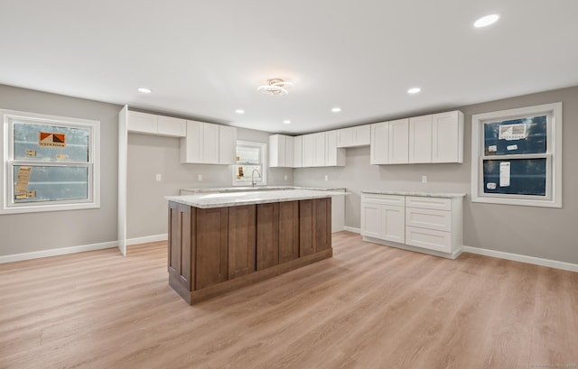 kitchen with white cabinets, a center island, light stone countertops, and light wood-type flooring