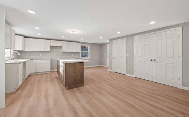 kitchen featuring sink, a kitchen island, light stone countertops, light hardwood / wood-style floors, and white cabinetry