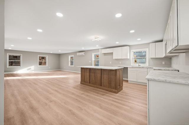 kitchen with white cabinetry, a wall mounted air conditioner, light stone counters, a kitchen island, and light wood-type flooring