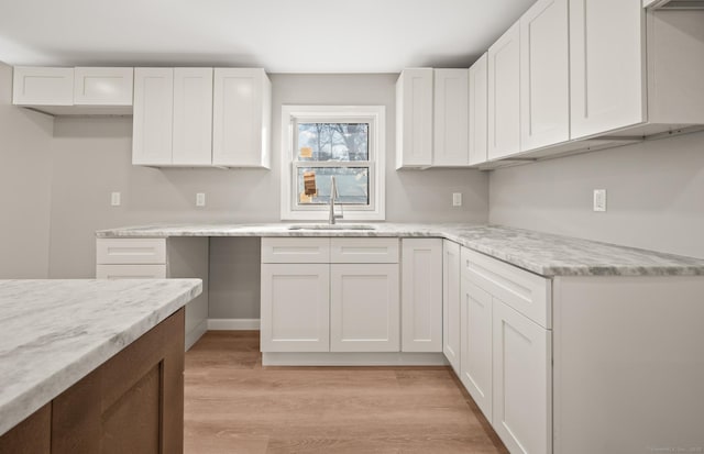 kitchen featuring light stone counters, white cabinetry, sink, and light hardwood / wood-style flooring