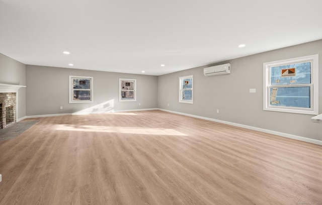 unfurnished living room featuring a fireplace, light hardwood / wood-style floors, and a wall mounted AC