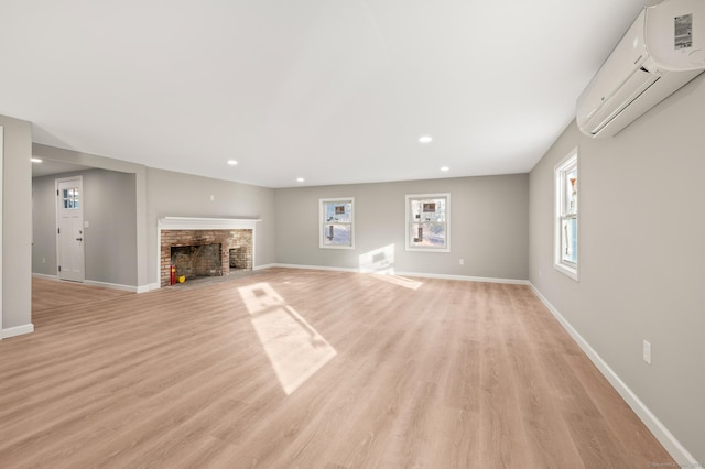 unfurnished living room with a wall mounted air conditioner, light hardwood / wood-style flooring, and a brick fireplace