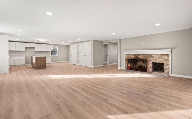 unfurnished living room featuring light hardwood / wood-style floors and a brick fireplace