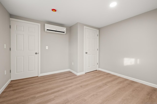 unfurnished bedroom with light wood-type flooring and an AC wall unit