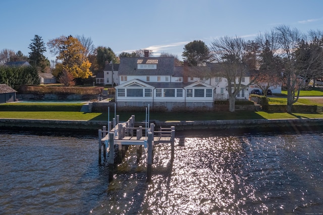 back of property with a water view, boat lift, and a lawn