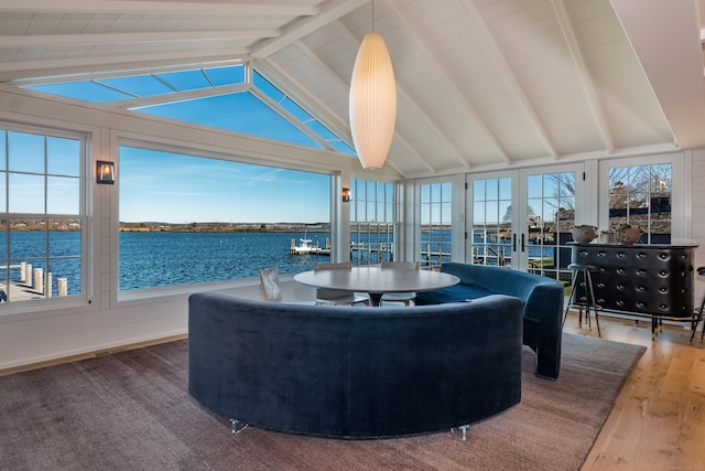 sunroom / solarium with a water view, lofted ceiling with beams, and french doors