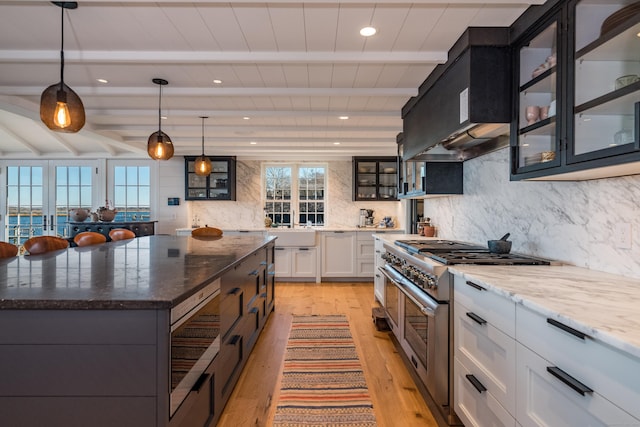 kitchen with dark stone counters, range with two ovens, glass insert cabinets, white cabinetry, and pendant lighting