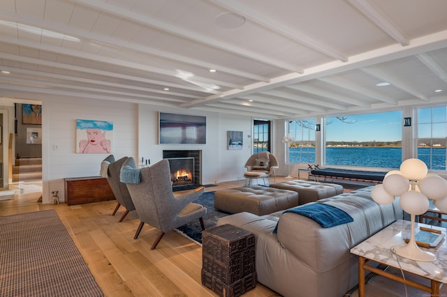 living room featuring light wood finished floors, a warm lit fireplace, and beamed ceiling