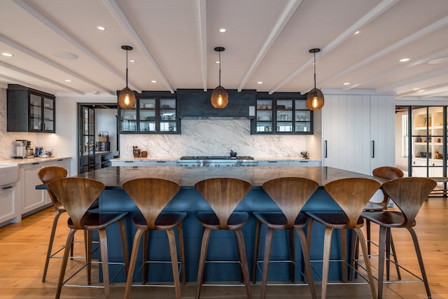 bar with beamed ceiling, light wood-type flooring, premium range hood, pendant lighting, and backsplash