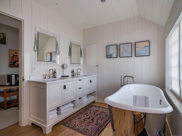 full bath featuring a sink, a healthy amount of sunlight, a freestanding bath, vaulted ceiling, and double vanity