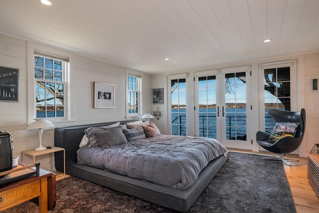 bedroom featuring access to outside, a water view, multiple windows, and wood finished floors