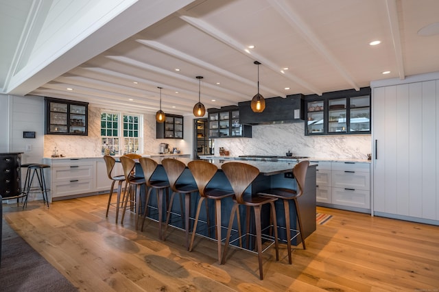 kitchen featuring beam ceiling, a large island, hanging light fixtures, glass insert cabinets, and white cabinets