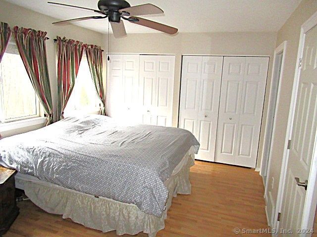 bedroom featuring ceiling fan, light wood-type flooring, and multiple closets