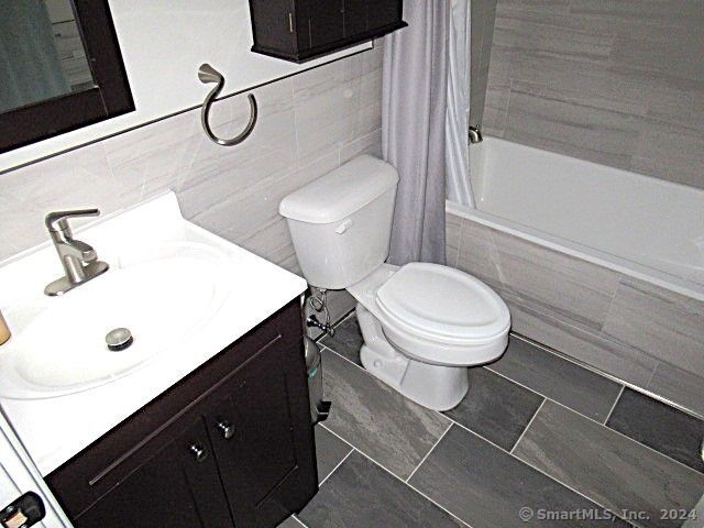 full bathroom with tile patterned floors, vanity, shower / tub combo with curtain, tile walls, and toilet