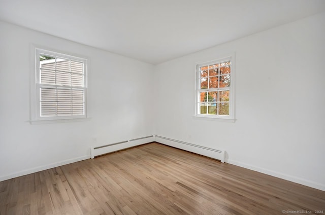 empty room with a wealth of natural light, light hardwood / wood-style floors, and a baseboard radiator